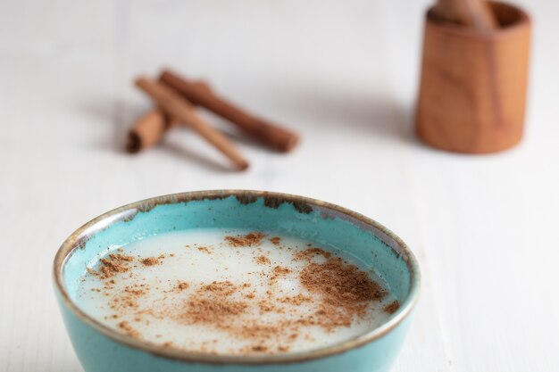 High angle shot of a cup of milk with cinnamon and some cinnamon sticks on a white surface