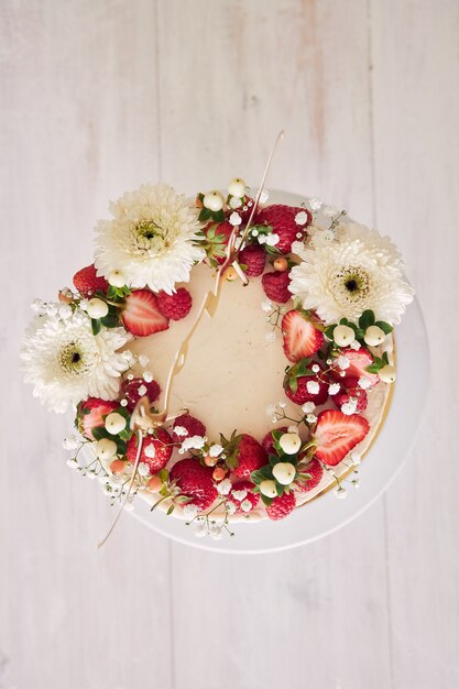 Высокий угол обзора восхитительного белого свадебного торта с красными ягодами и цветами на белом деревянном столе
