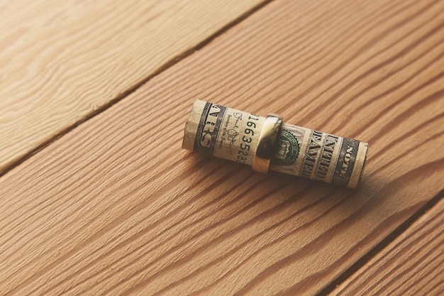 High angle shot of dollar bills rolled in a golden ring on a wooden surface