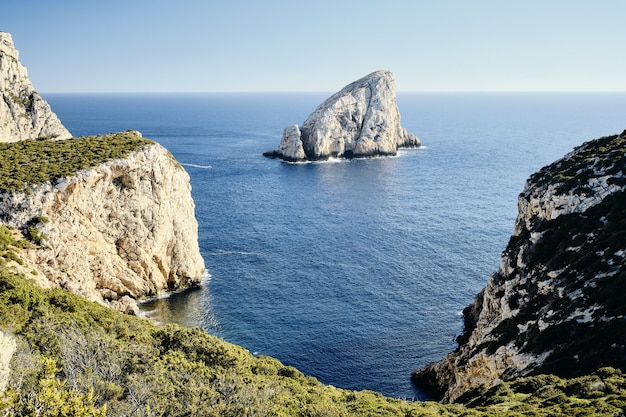 High angle shot of grassy cliffs near the sea with a rock in the distance