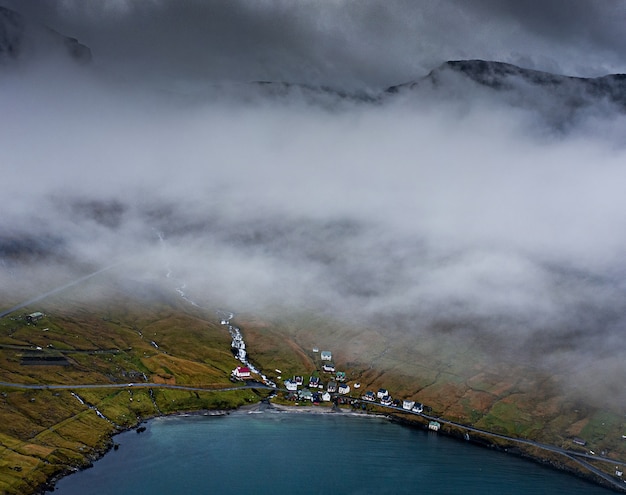 Free photo high angle shot of houses on a grass-covered hill by the water captured on a foggy evening