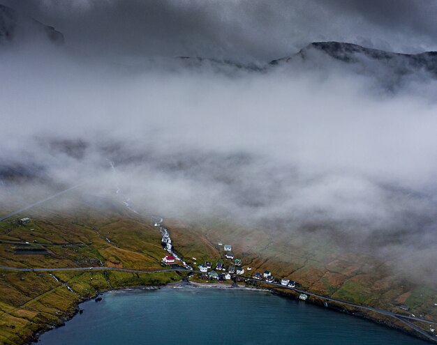 High angle shot of houses on a grass-covered hill by the water captured on a foggy evening