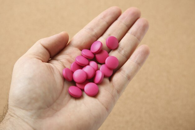 Снимок руки человека с горсткой розовых таблеток под высоким углом
