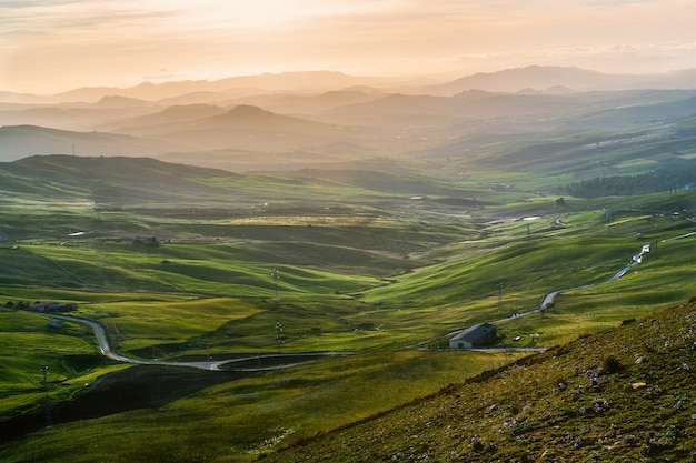 High angle shot of an isolated building in a green field surrounded by high mountains