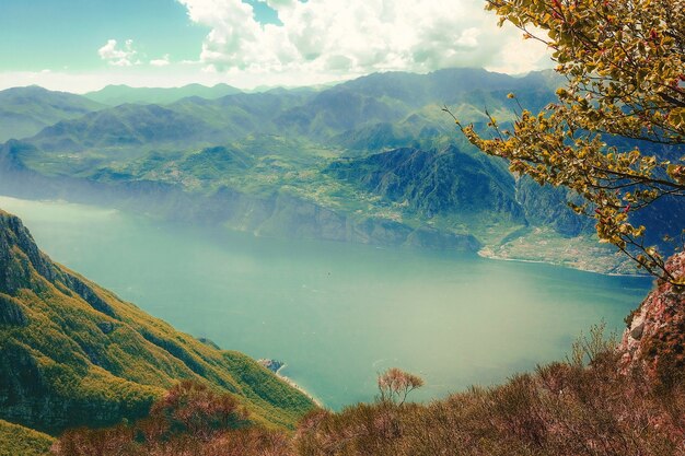 High angle shot of a lake surrounded by green mountains covered in fog under the cloudy sky