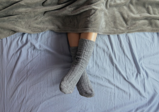 Free photo high angle shot of the legs of a female in grey knitted socks under the blanket