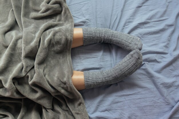 High angle shot of the legs of a female in grey knitted socks under the blanket
