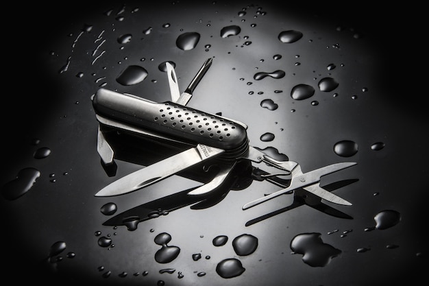 High angle shot of metal multi-purpose knife with water droplets isolated on black surface
