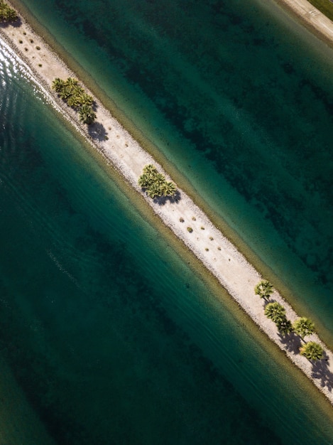 High angle shot of a narrow sand line with green trees in the middle of the sea