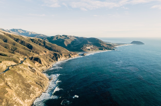 High angle shot of the ocean at a rock formation covered in greenery