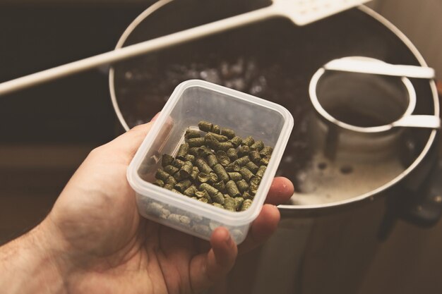 High angle shot of a person holding a bowl of some herbs over a pot on the stove