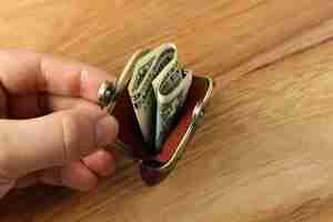 Free photo high angle shot of a person holding a change purse with some cash in it over a wooden surface