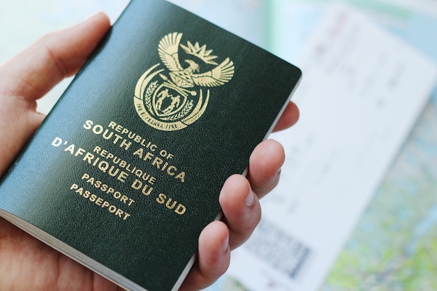 High angle shot of a person holding a passport over a plane ticket and a geographical map