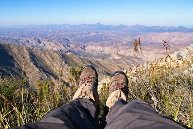 아름다운 계곡 너머 언덕 꼭대기에 앉아있는 사람의 발의 높은 각도 샷