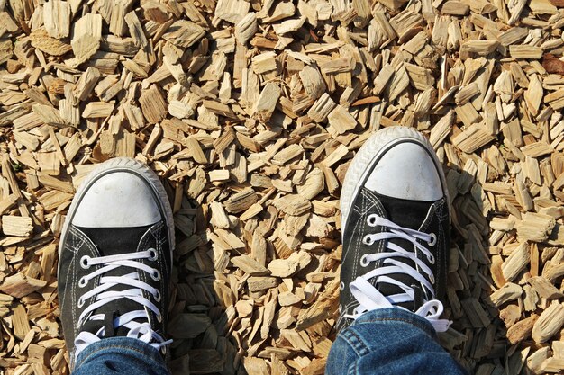 High angle shot of a person's feet standing on the ground covered with chops of wood