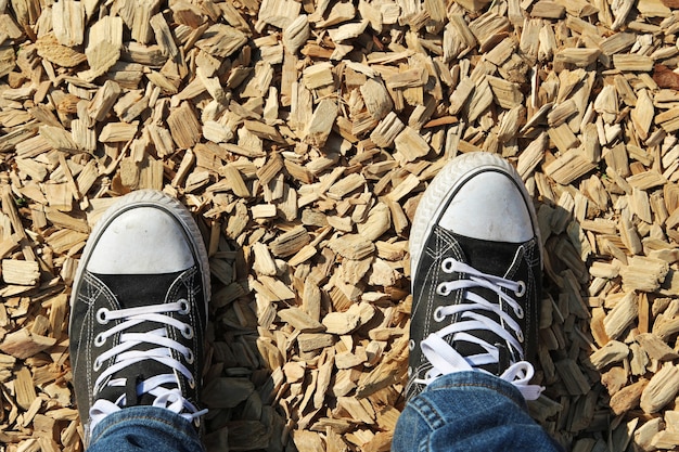 Снимок под высоким углом ног человека, стоящего на земле, покрытой деревянными щепками.