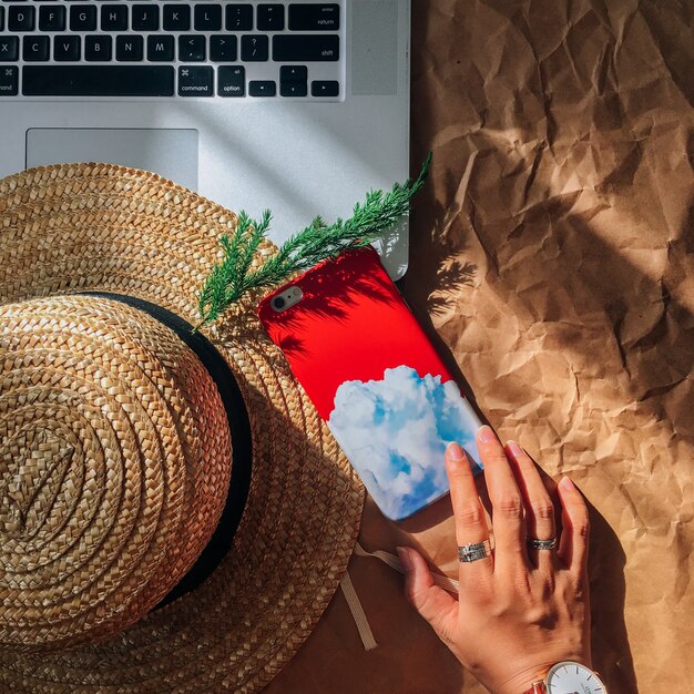 High angle shot of a person's hand with silver rings near a laptop, a phone and a hat