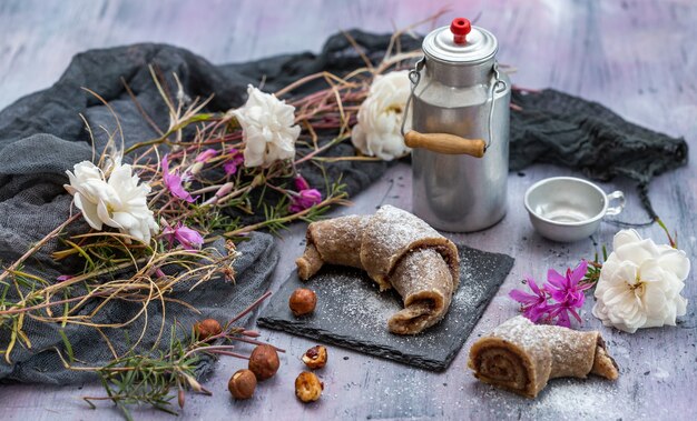 High angle shot of raw vegan rolls, hazelnuts, an aluminum milk bottle, and white and pink flowers