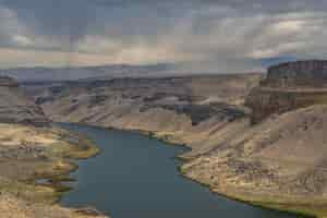 Free photo high angle shot of a river in the middle of cliffs with mountains and a cloudy sky