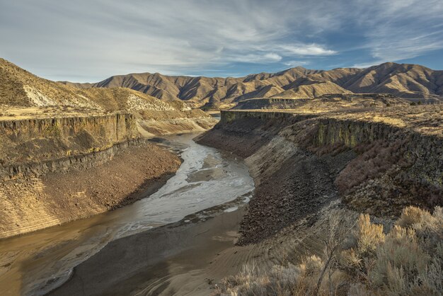 High angle shot of a river in the middle of cliffs with mountains in the distance under a blue sky