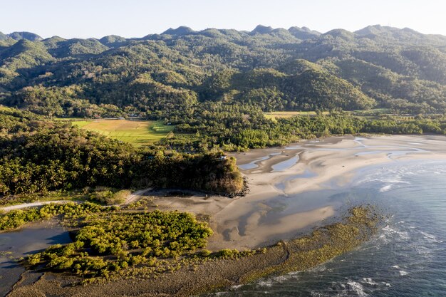 High angle shot of a sea near a shore and mountains covered in trees at daytime