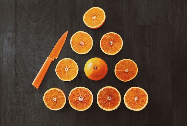 Free photo high angle shot of sliced oranges in a triangle shape beside an orange knife on a black surface