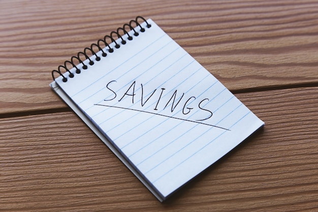 Free photo high angle shot of a small notebook with the word savings written on it on a wooden surface