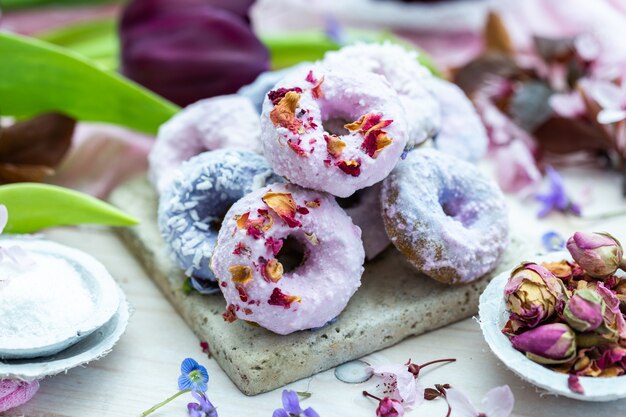 Снимок синих и фиолетовых веганских пончиков под высоким углом в окружении цветов на столе