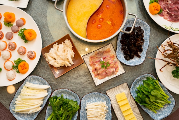 High angle shot of soup near a plate with raw meat with a side dishes