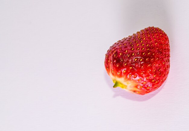 High angle shot of a strawberry on a white surface under the lights