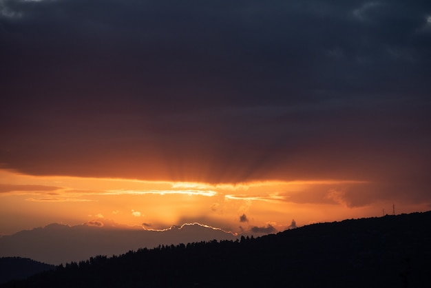 山の向こうの暗い空に沈む夕日のハイアングルショット