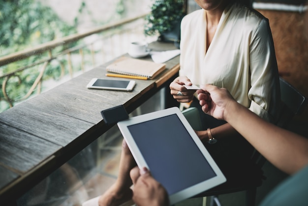 Free photo high angle shot of unrecognizable waiter with tablet accepting credit card from woman in cafe