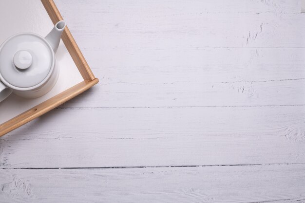 High angle shot of a white teapot on a tray on a white wooden table