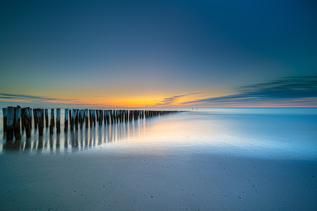 Foto gratuita colpo di alto angolo di un ponte di legno in riva al mare che conduce al mare al tramonto