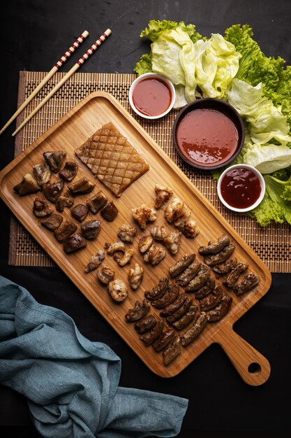 High angle shot of a wooden tray of fried meat, potatoes, vegetables, and sauce on a black table
