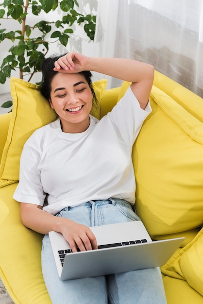 High angle of smiley woman at home on couch with laptop