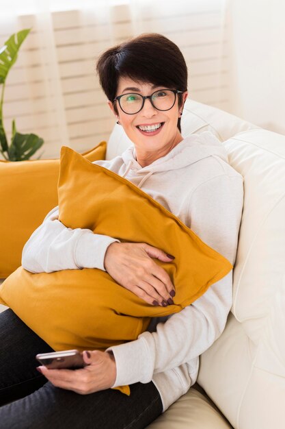 High angle of smiley woman on sofa with smartphone