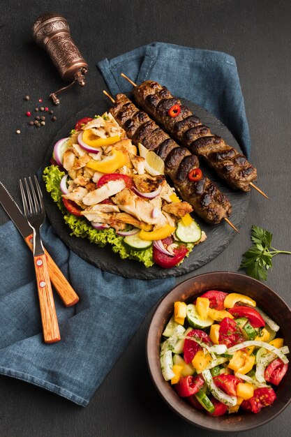 High angle of tasty kebab on slate with other dish and cutlery