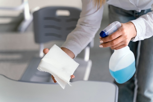 High angle of teacher disinfecting school benches in classroom