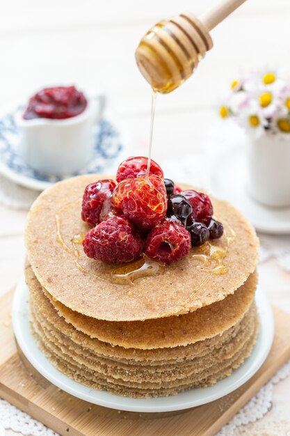 High angle vertical closeup shot of raw vegan pancakes with honey and berries