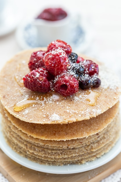 High angle vertical closeup shot of raw vegan pancakes with honey and berries