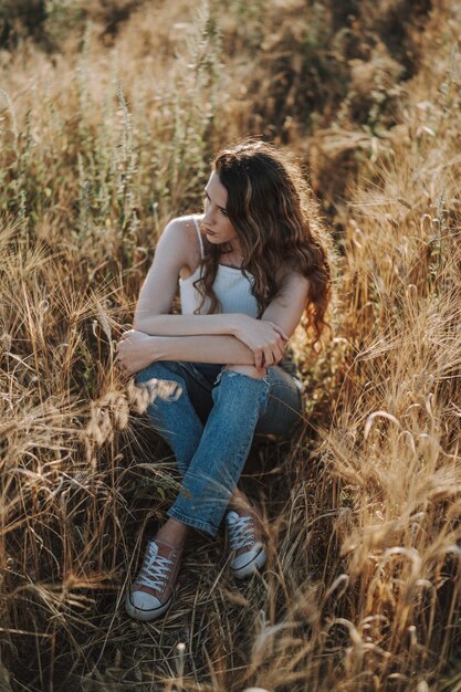 High angle vertical shot of a beautiful blonde Spanish girl sitting cross-legged in a wheat field