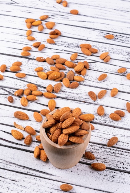 Free photo high angle view almond in wooden cup on white wooden table. vertical