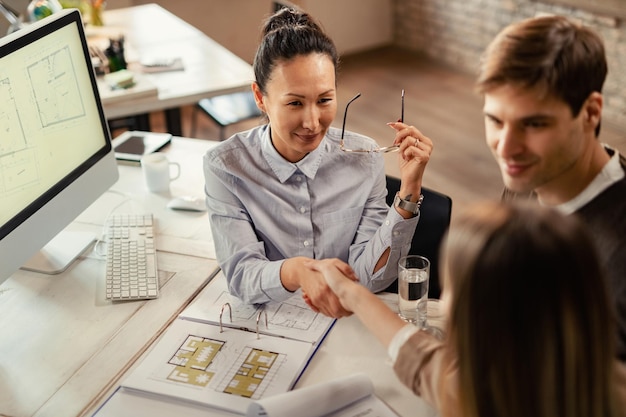 Vista ad alto angolo del consulente finanziario asiatico che stringe la mano con i suoi clienti durante una riunione in ufficio