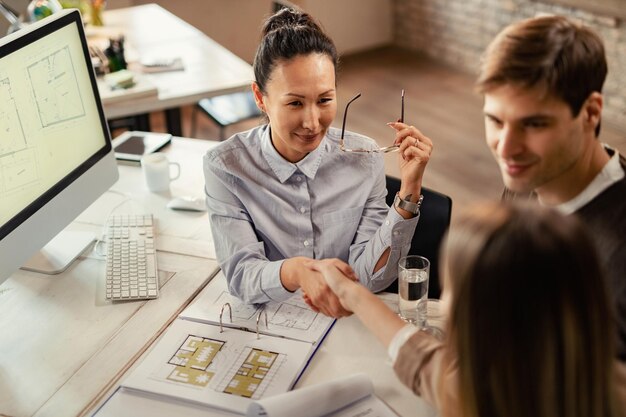 High angle view of Asian financial advisor handshaking with her clients on a meeting in the office