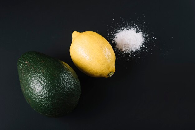 High angle view of avocado; lemon and salt on black background