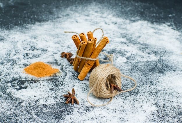 High angle view a ball of rope tied to dry cinnamon with cinnamon powder on gray textured surface. horizontal