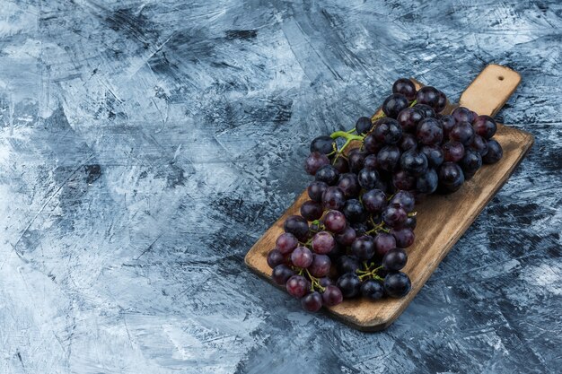 汚れた石膏とまな板の背景に黒ブドウを高角度で表示します。水平