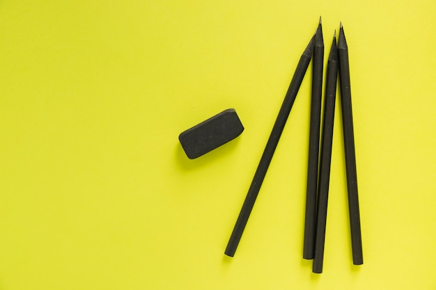 High angle view of black pencils and eraser on yellow background