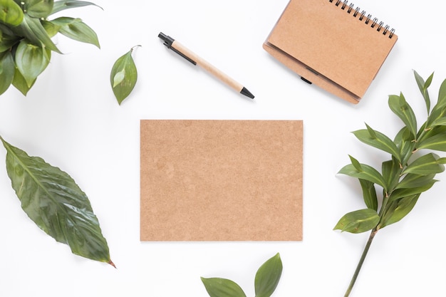 Free photo high angle view of blank brown papers; leaves; diary and pen on white surface